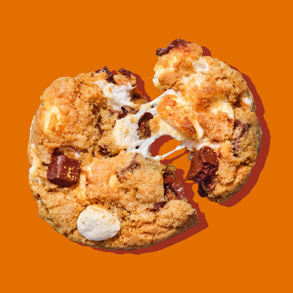 Bakr Smores cookie broken in half with gooey chocolate chunk and marshmallows on orange background